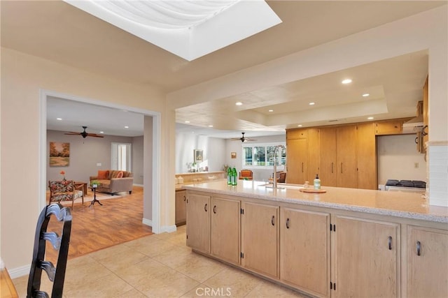 kitchen featuring kitchen peninsula, light brown cabinets, light tile patterned floors, and a raised ceiling