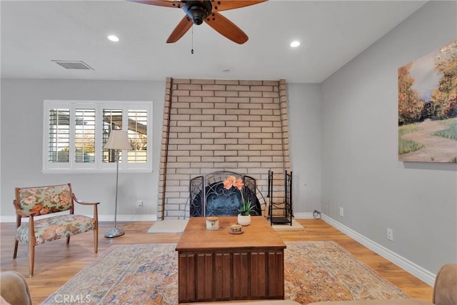 living room featuring ceiling fan, light wood-type flooring, and a brick fireplace