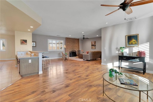 living room featuring ceiling fan, light hardwood / wood-style flooring, a healthy amount of sunlight, and a brick fireplace