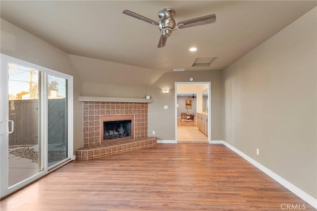 unfurnished living room featuring ceiling fan, lofted ceiling, light wood-type flooring, and a tiled fireplace