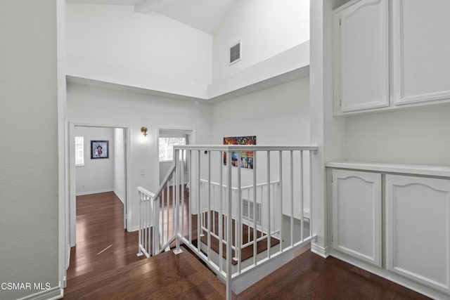 stairs featuring beam ceiling, wood-type flooring, and high vaulted ceiling