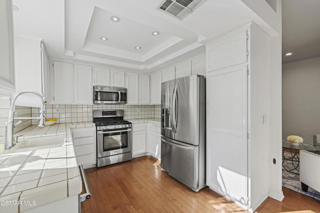 kitchen with sink, stainless steel appliances, a tray ceiling, white cabinets, and tile countertops