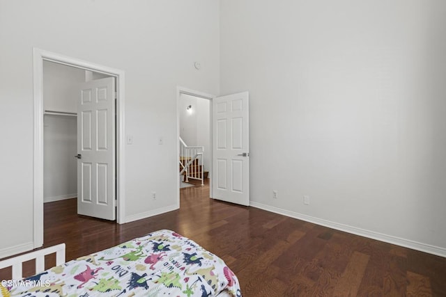 bedroom featuring dark wood-type flooring, a towering ceiling, a closet, and a walk in closet