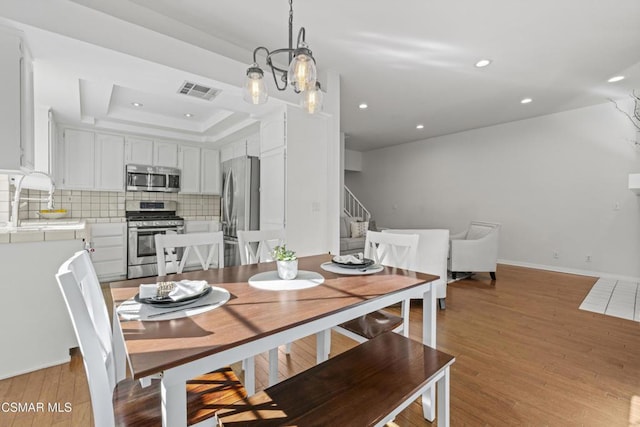 dining area with light hardwood / wood-style flooring, a raised ceiling, and a chandelier