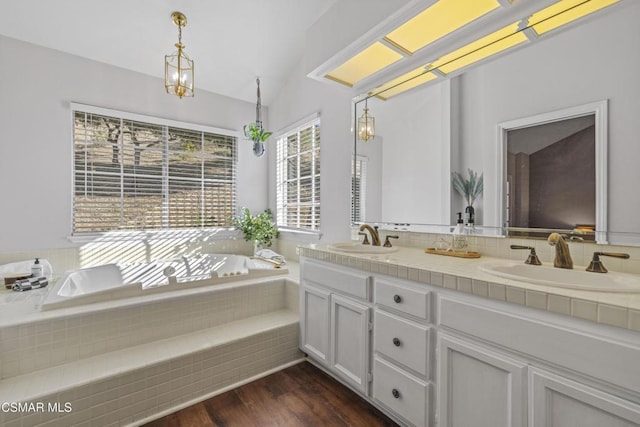 bathroom with hardwood / wood-style flooring, an inviting chandelier, a relaxing tiled tub, vanity, and vaulted ceiling