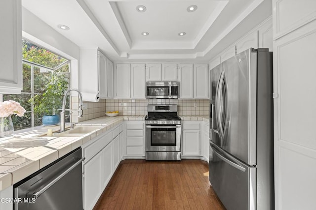 kitchen featuring sink, stainless steel appliances, a tray ceiling, white cabinets, and tile countertops