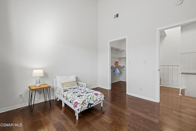 bedroom featuring a high ceiling, a spacious closet, dark hardwood / wood-style flooring, and a closet