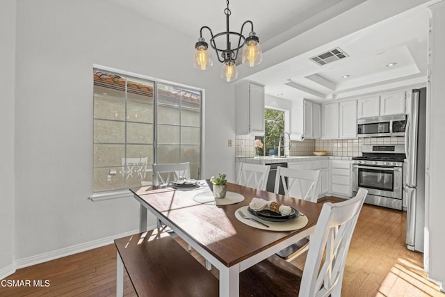 dining area with sink, a tray ceiling, wood-type flooring, and a notable chandelier