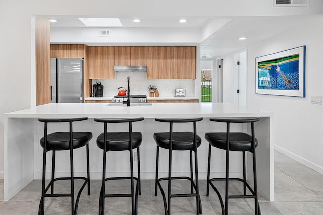 kitchen with stainless steel refrigerator, sink, tasteful backsplash, a kitchen bar, and a center island with sink