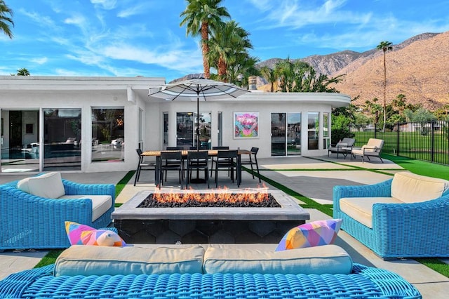 back of property with a mountain view, a patio, and an outdoor living space with a fire pit