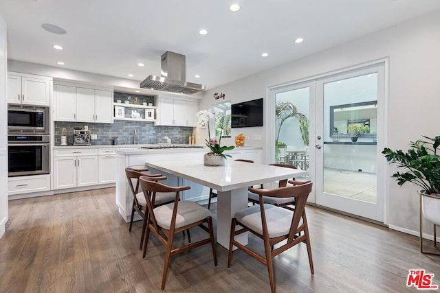 kitchen featuring hardwood / wood-style floors, tasteful backsplash, white cabinetry, island exhaust hood, and stainless steel appliances