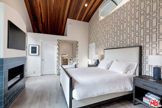 bedroom featuring a tiled fireplace, hardwood / wood-style floors, high vaulted ceiling, and wooden ceiling