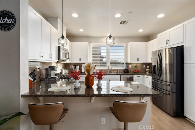 kitchen featuring visible vents, stainless steel appliances, a kitchen bar, and white cabinetry