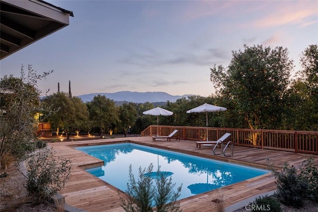 pool at dusk featuring a deck with mountain view