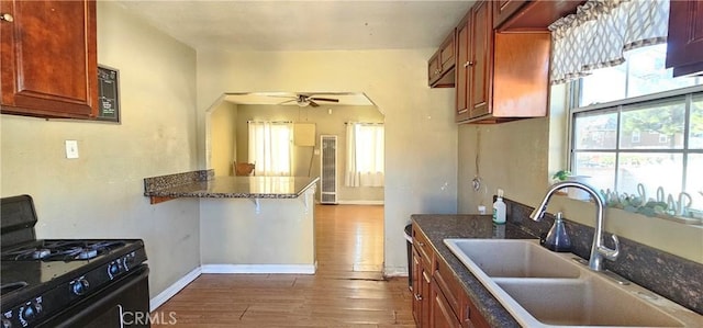 kitchen with kitchen peninsula, dark hardwood / wood-style floors, ceiling fan, black gas range, and sink