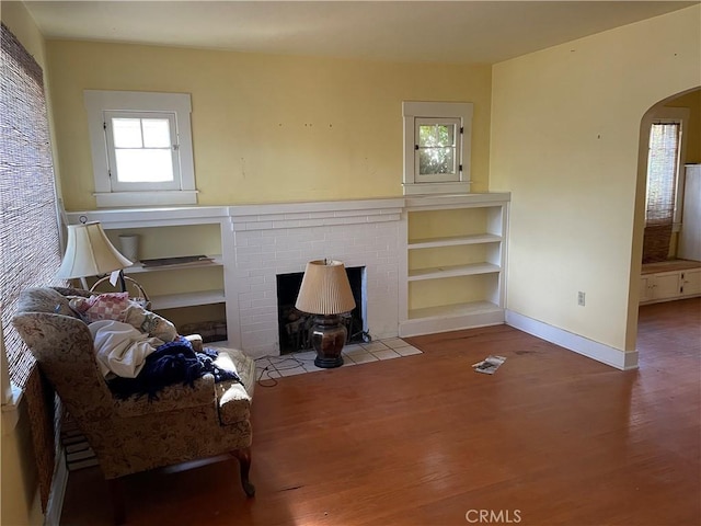 living room with hardwood / wood-style flooring, built in features, and a brick fireplace