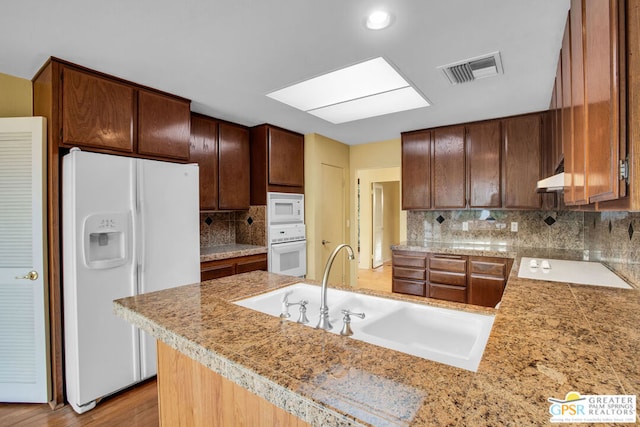 kitchen with kitchen peninsula, white appliances, backsplash, and sink