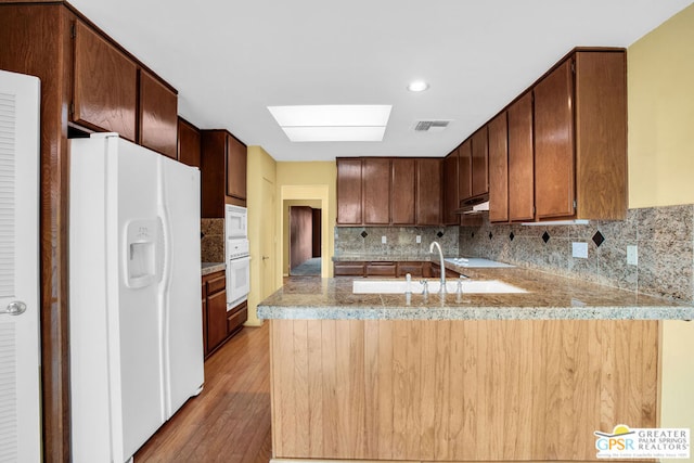 kitchen with white appliances, sink, decorative backsplash, light wood-type flooring, and kitchen peninsula