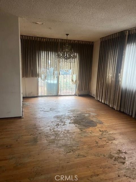 unfurnished dining area with a textured ceiling, an inviting chandelier, and hardwood / wood-style floors