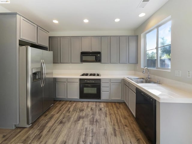 kitchen featuring dark wood-type flooring, black appliances, gray cabinetry, and sink