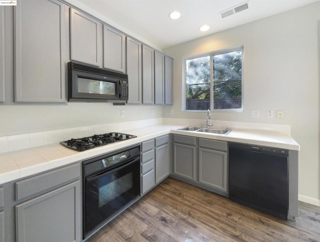 kitchen with black appliances, gray cabinetry, sink, and tile counters