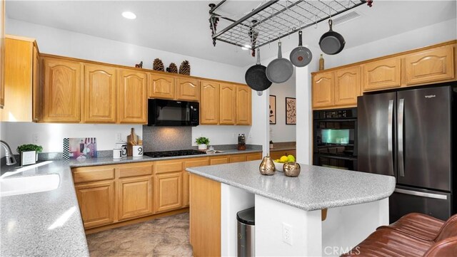 kitchen with black appliances, light tile patterned floors, a kitchen island, sink, and backsplash