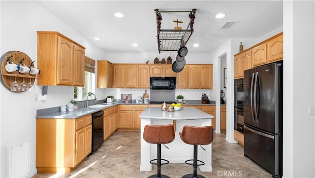 kitchen featuring a sink, black appliances, a breakfast bar area, visible vents, and a kitchen island