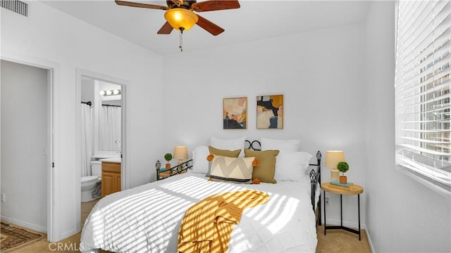 bedroom featuring visible vents, baseboards, light colored carpet, ceiling fan, and ensuite bathroom