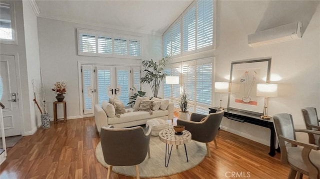 living room with a wall mounted AC, a wealth of natural light, a towering ceiling, and hardwood / wood-style flooring