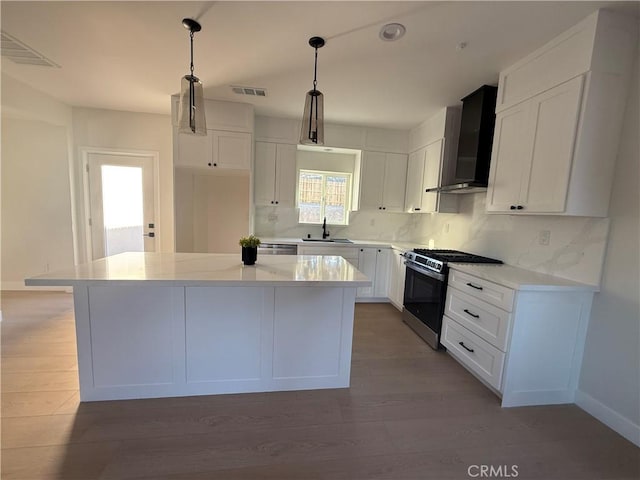 kitchen with gas range, a kitchen island, wall chimney range hood, pendant lighting, and white cabinetry