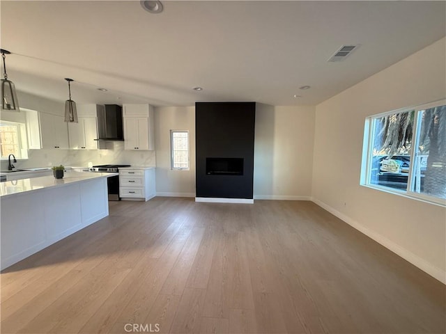 kitchen featuring stainless steel range, sink, wall chimney range hood, pendant lighting, and white cabinets