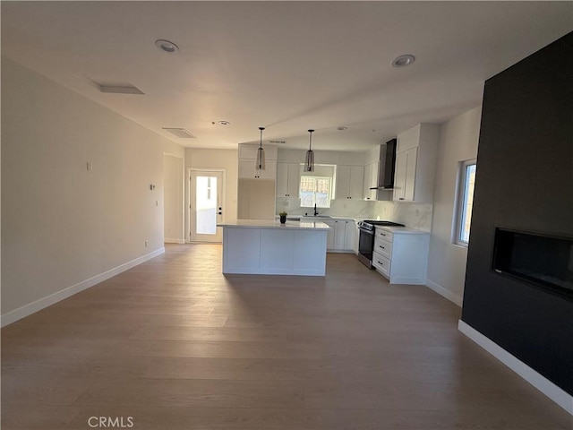 kitchen with a center island, white cabinets, wall chimney exhaust hood, decorative light fixtures, and gas stove