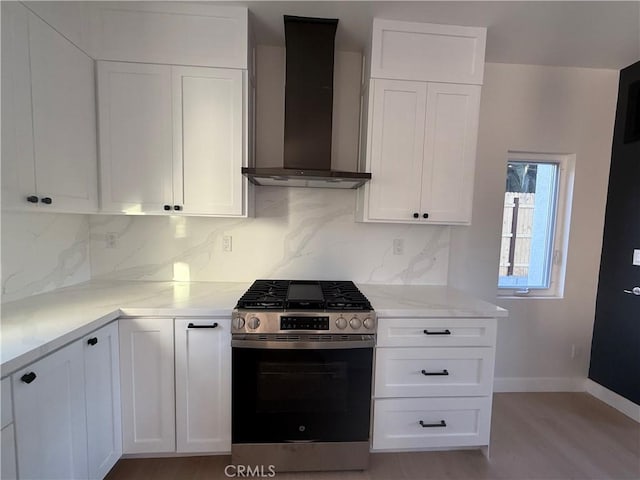 kitchen featuring stainless steel gas range oven, wall chimney exhaust hood, decorative backsplash, light stone countertops, and white cabinetry