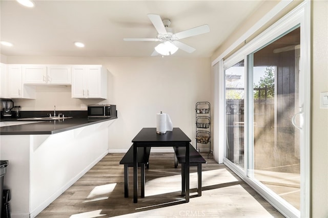 kitchen featuring kitchen peninsula, ceiling fan, white cabinetry, wood-type flooring, and a breakfast bar area