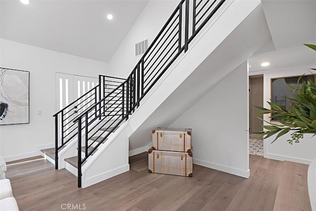 stairs with high vaulted ceiling and wood-type flooring