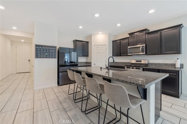 kitchen featuring stainless steel appliances, sink, a center island with sink, dark stone countertops, and a breakfast bar area