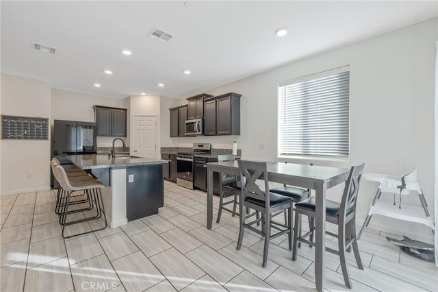 kitchen featuring dark brown cabinetry, sink, an island with sink, a kitchen bar, and appliances with stainless steel finishes