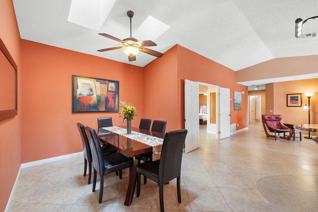 tiled dining area featuring ceiling fan and vaulted ceiling with skylight