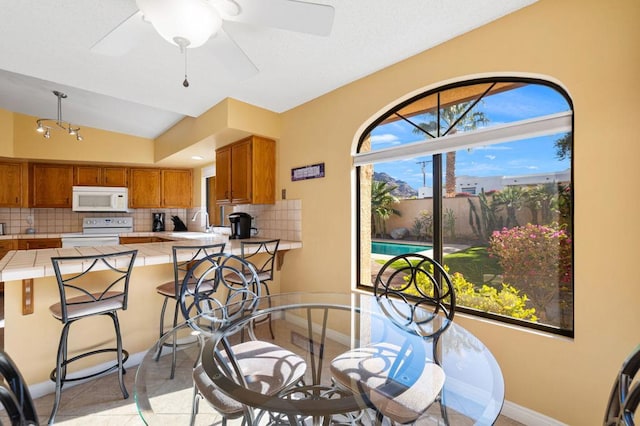 dining room with ceiling fan, vaulted ceiling, sink, and light tile patterned floors