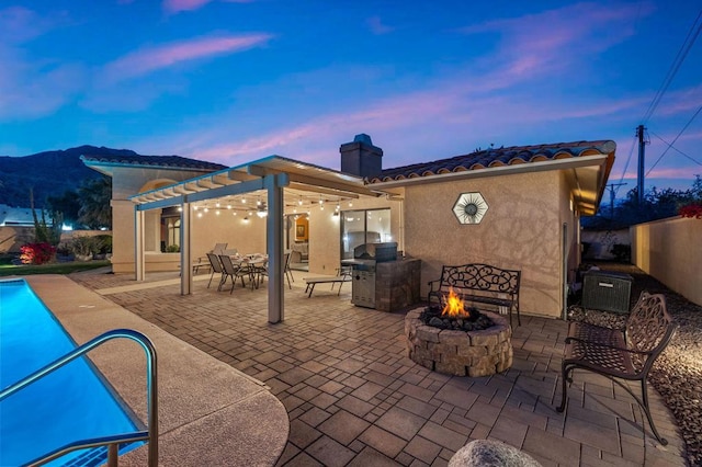 back house at dusk featuring a fire pit, a mountain view, a pergola, and a patio