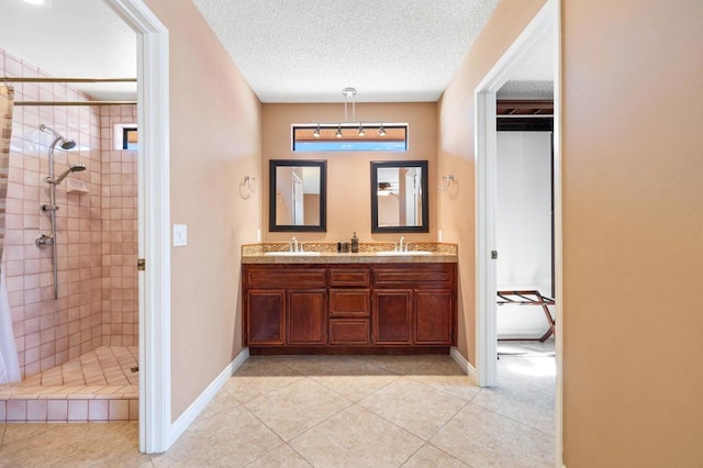 bathroom featuring a textured ceiling, tiled shower, tile patterned flooring, and vanity