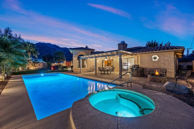 pool at dusk featuring an outdoor fire pit, a patio area, an in ground hot tub, and grilling area