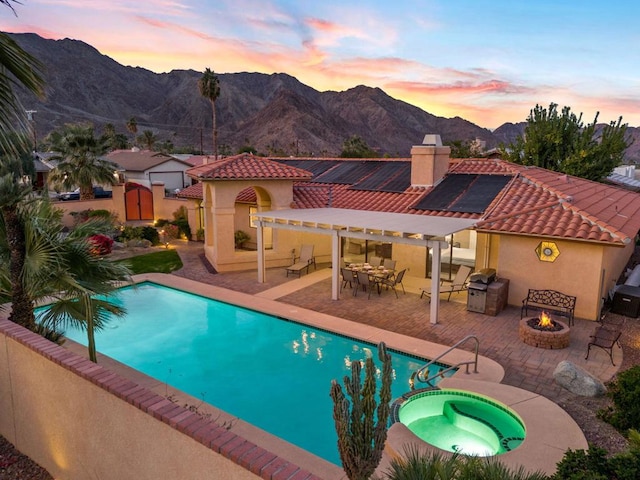 pool at dusk featuring a patio, a fire pit, an in ground hot tub, and a mountain view