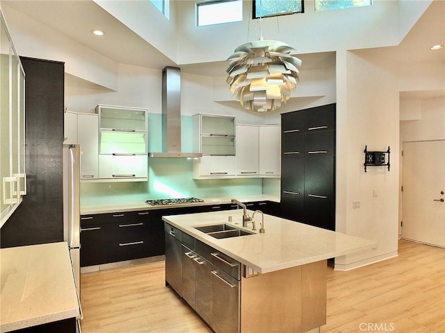 kitchen with sink, white cabinetry, a high ceiling, an island with sink, and wall chimney exhaust hood