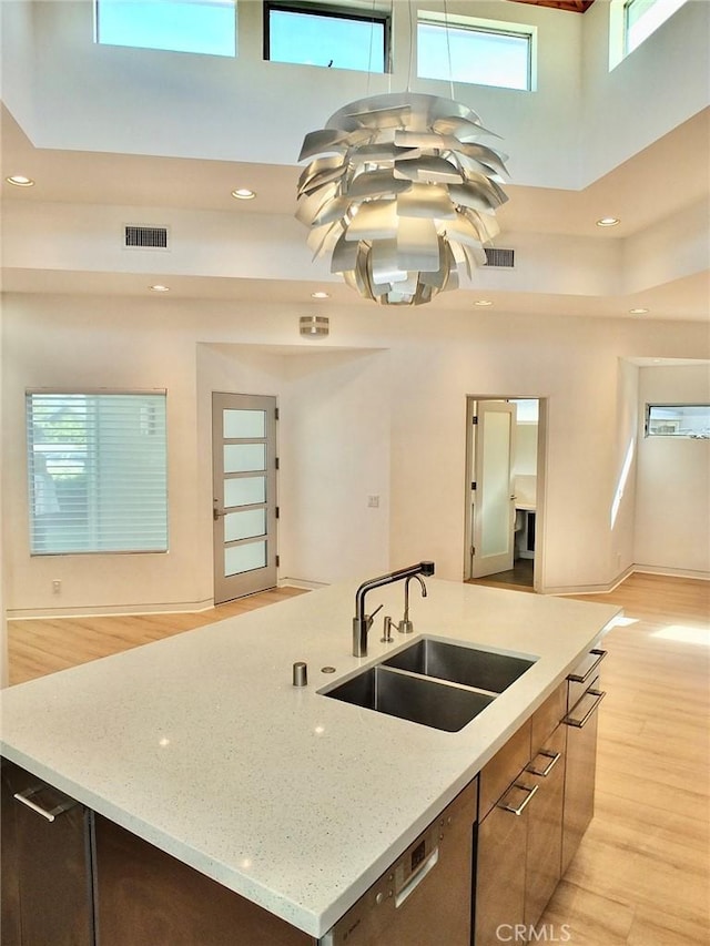 kitchen featuring light stone countertops, a towering ceiling, sink, and light hardwood / wood-style floors