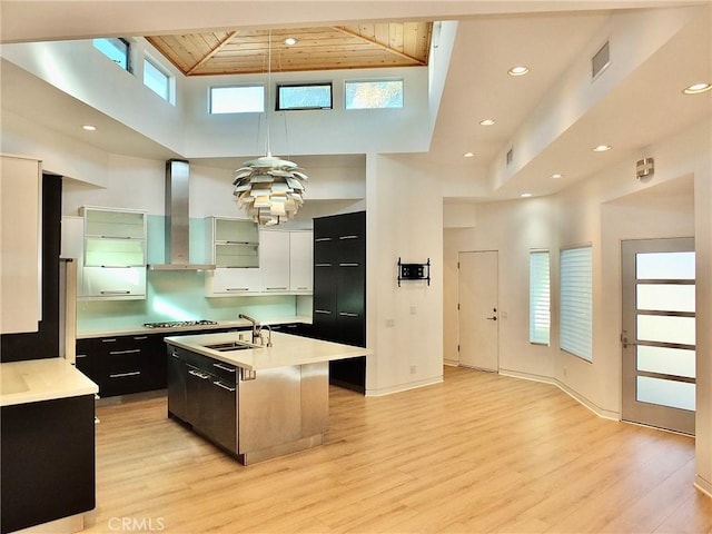 kitchen featuring sink, wood ceiling, hanging light fixtures, a center island with sink, and wall chimney exhaust hood