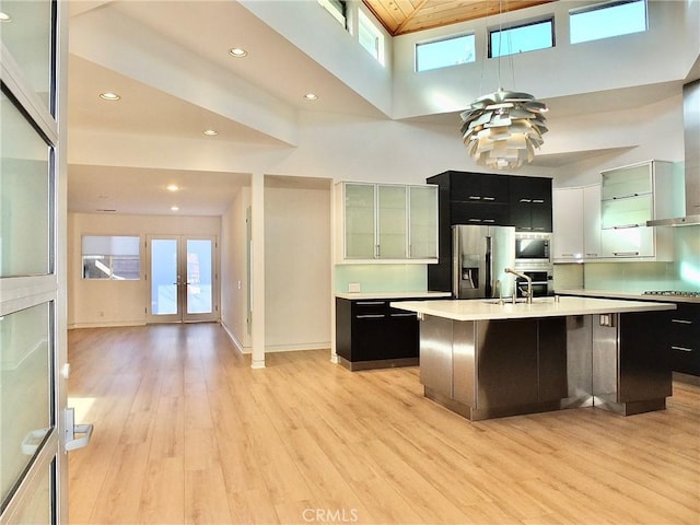 kitchen with a breakfast bar, a high ceiling, stainless steel appliances, a center island with sink, and light hardwood / wood-style flooring