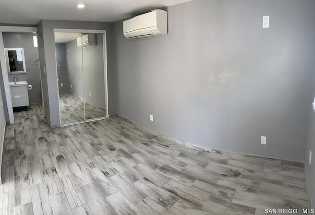 unfurnished bedroom with light wood-type flooring, a closet, sink, and a wall mounted air conditioner