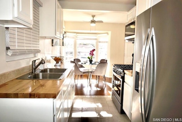 kitchen with white cabinets, wooden counters, stainless steel appliances, sink, and ceiling fan