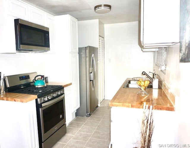 kitchen featuring light tile patterned floors, butcher block countertops, appliances with stainless steel finishes, white cabinets, and sink